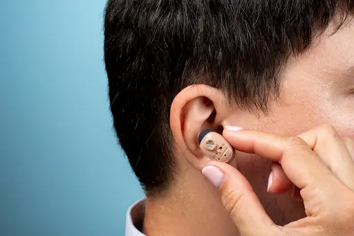 Close-up of a person inserting a beige behind-the-ear hearing aid into their ear.
